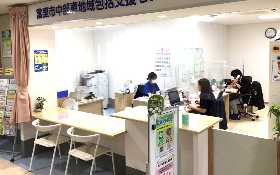 介護施設の受付・ロビー。スタッフが対応し、待合座席と事務作業スペースがある